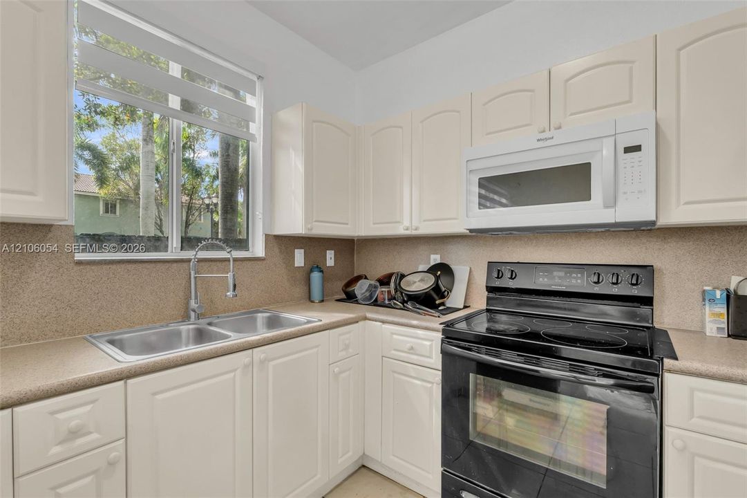 Kitchen featuring white cabinetry, solid-surface countertops, dual-basin stainless steel sink with pull-down faucet, and integrated black electric range and microwave
