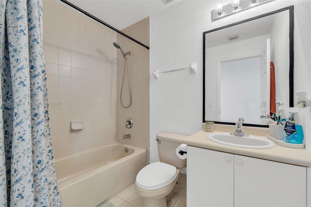Bathroom featuring a built-in vanity with a solid-surface countertop and integrated sink, a full-wall mirror with a black frame, and a tub-shower combination with tiled surround