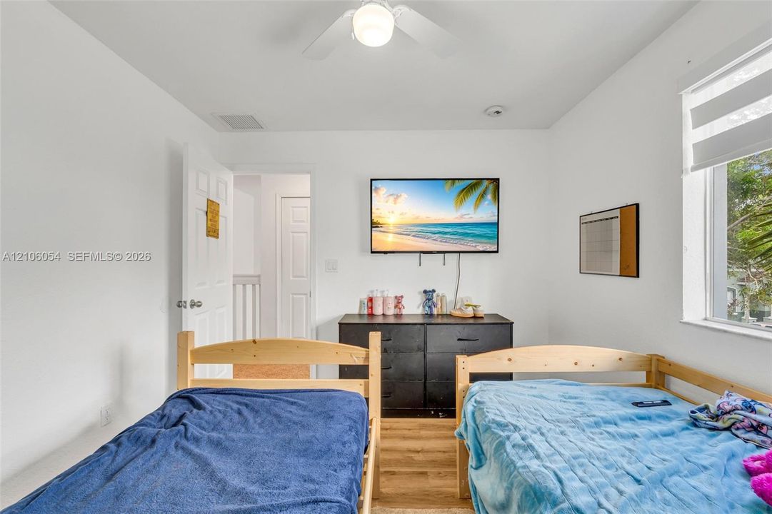 Neutral interior space featuring wood-finish flooring, a ceiling fan with integrated lighting, and a window with a roller shade