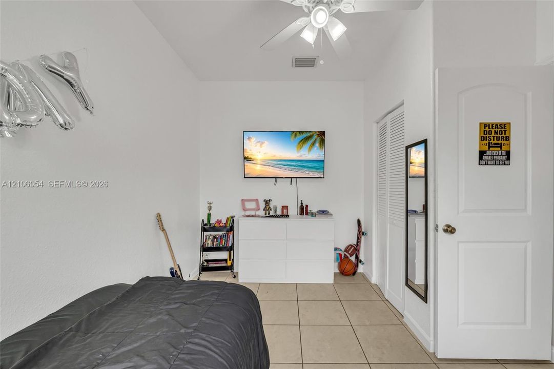 Neutral-toned tile flooring, white-finish walls, ceiling-mounted light fixture with fan, and closet with louvered doors