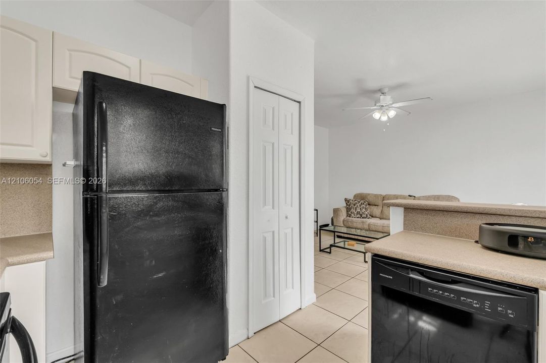 Kitchen featuring off-white cabinetry, solid-surface countertops, black appliances, tile flooring, and a ceiling fan with integrated lighting