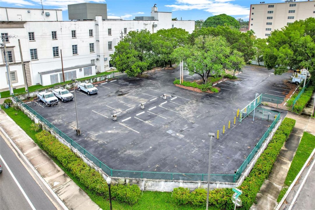 Asphalt-paved surface parking lot featuring perimeter chain-link fencing, painted parking stalls, and mature trees