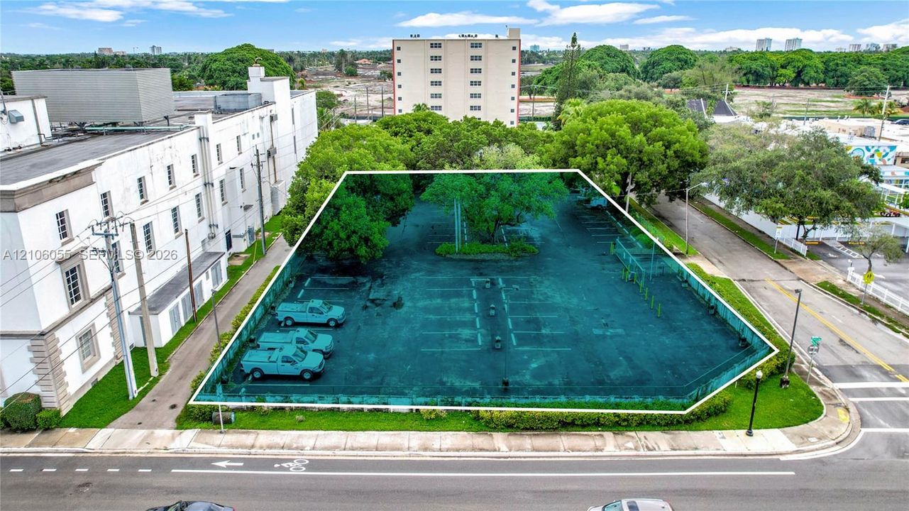 Corner lot featuring paved surface parking, established trees, and perimeter landscaping