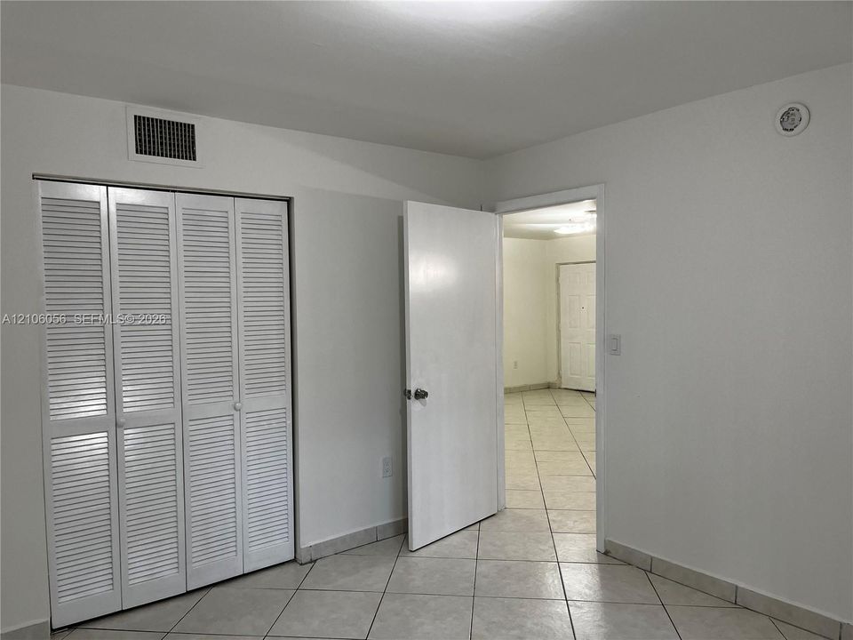 Neutral-toned tile flooring, white interior doors, and a four-panel louvered closet door
