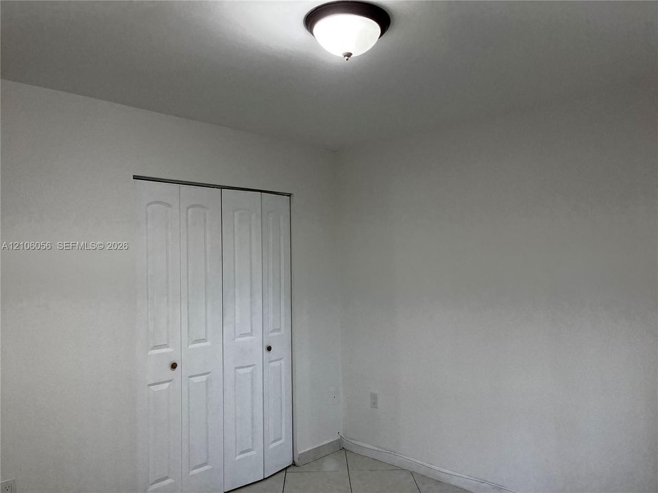 Neutral-toned interior space featuring tile flooring, white walls, a flush-mount ceiling light fixture, and a white bi-fold closet door