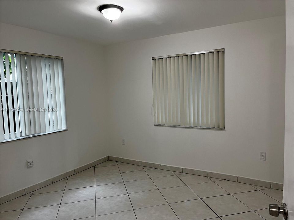 Neutral-toned tile flooring, dual windows with vertical blinds, and a semi-flush mount ceiling fixture