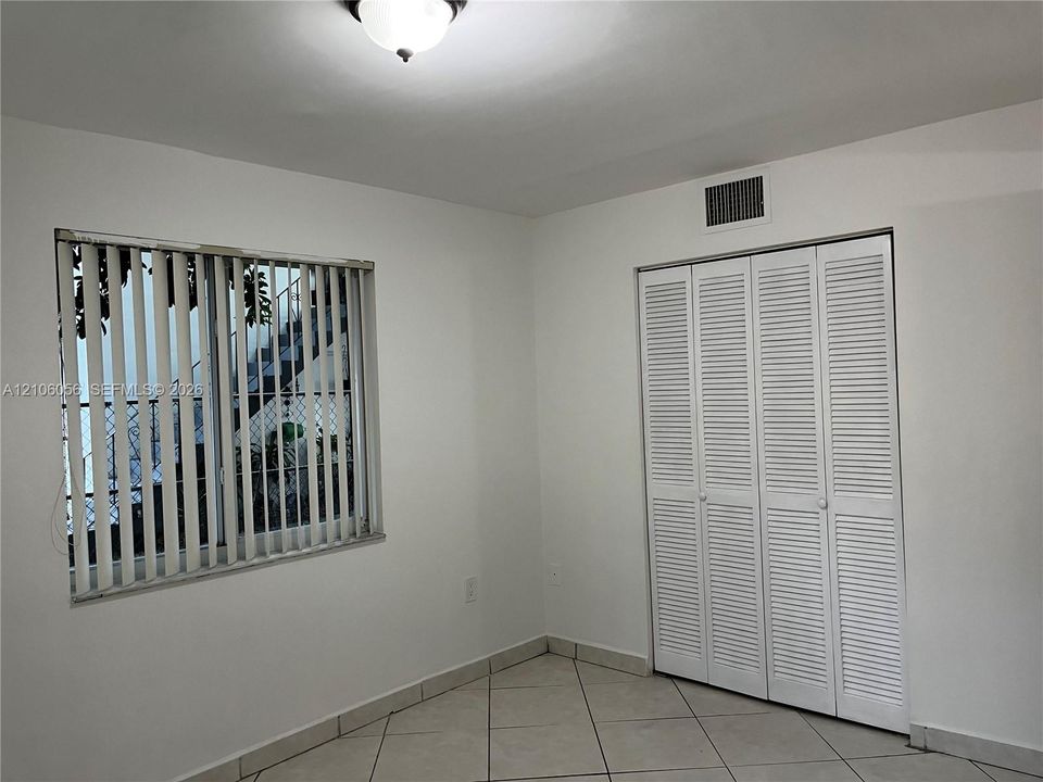 Interior space featuring neutral wall tones, large-format tile flooring, a window with vertical blinds, and a built-in closet with louvered bifold doors