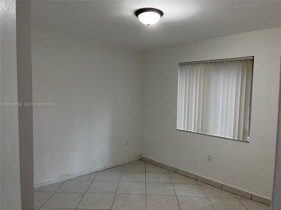 Neutral-toned interior space featuring light-colored tile flooring, smooth wall finishes, a centered dome light fixture, and vertical window blinds
