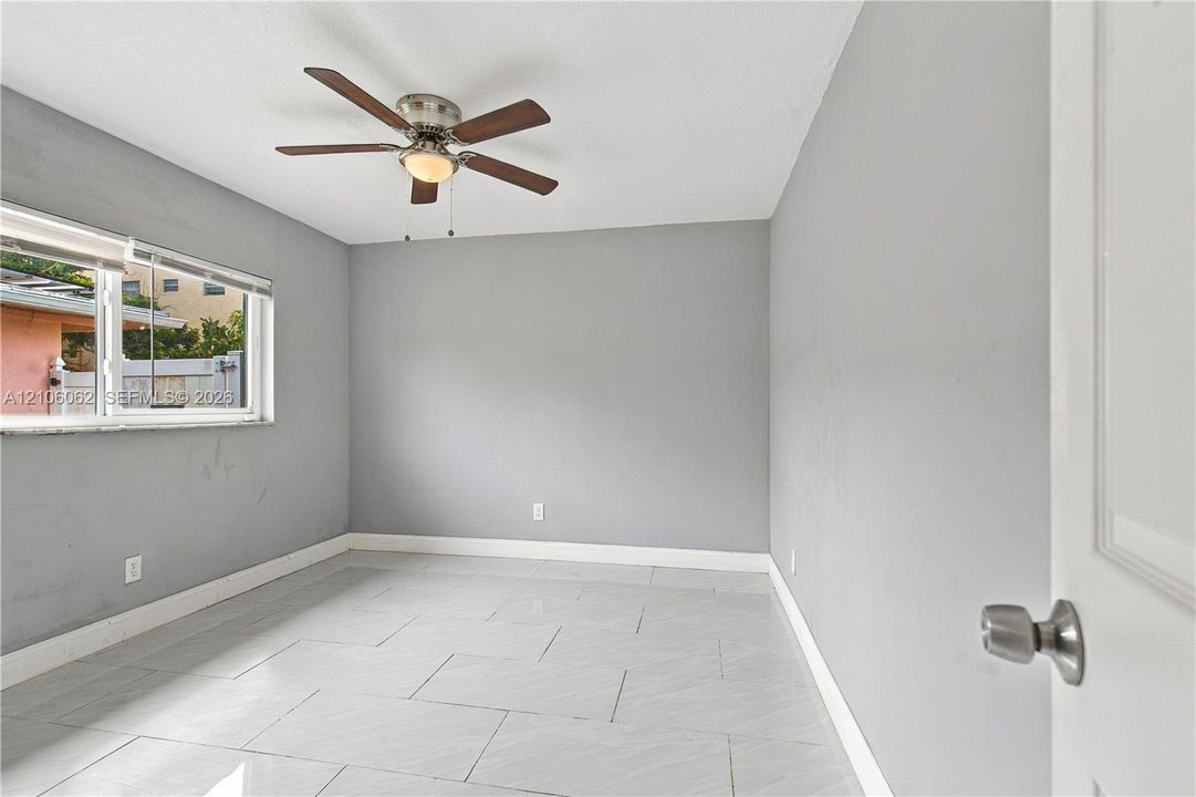 Neutral-toned interior space featuring rectangular tile flooring, a multi-blade ceiling fan with integrated lighting, and a horizontal window
