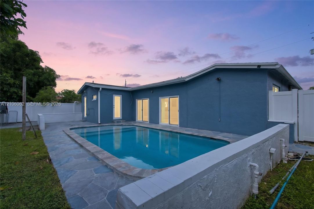 Rear exterior featuring an in-ground swimming pool, flagstone patio, white privacy fencing, and two sets of sliding glass doors