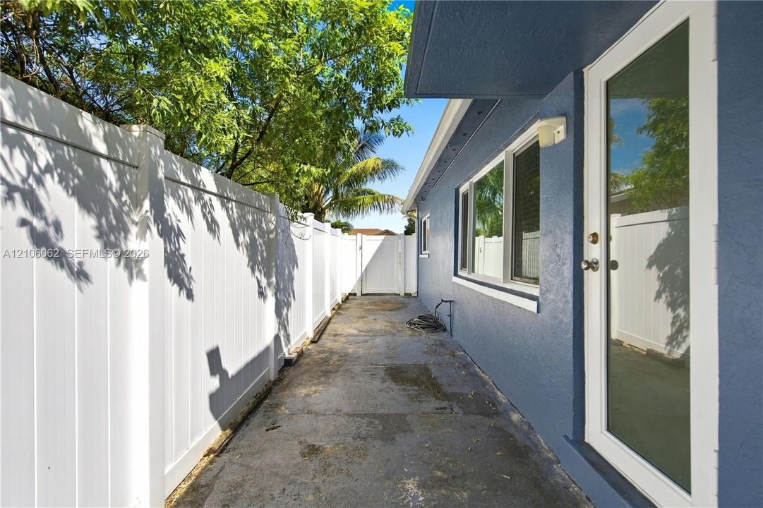 Concrete side yard featuring a white vinyl privacy fence and a glass-paneled exterior door