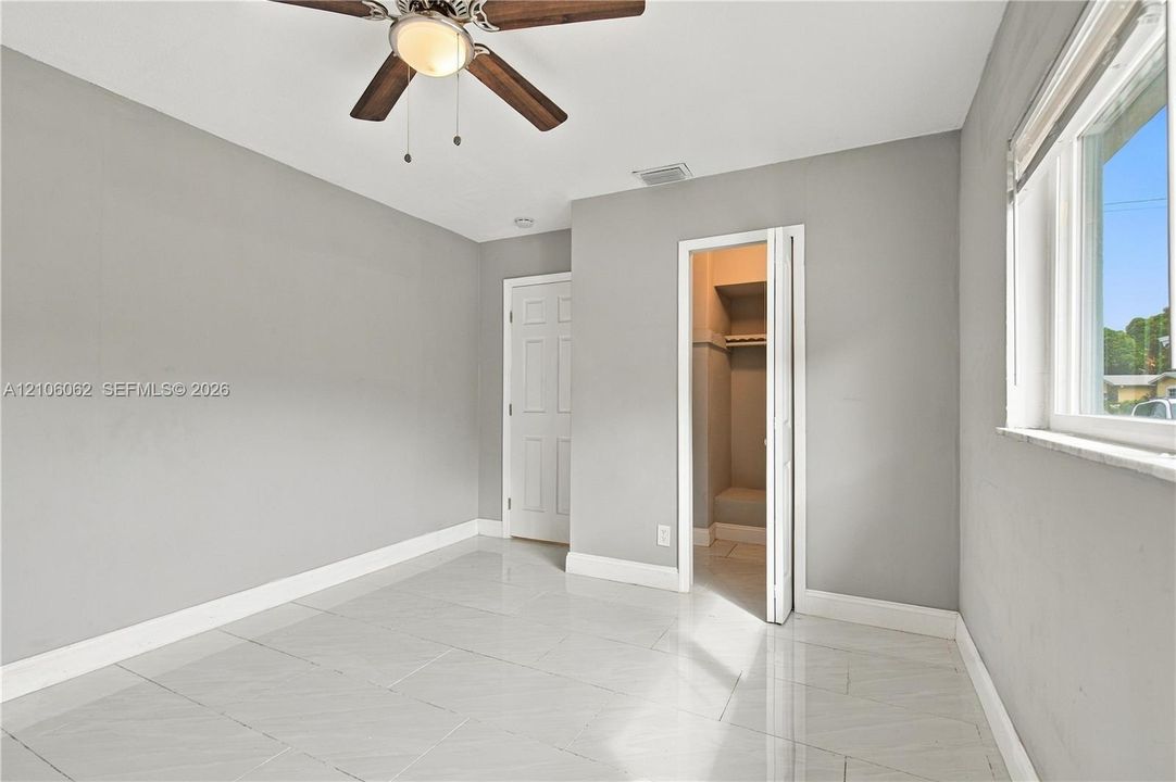 Neutral-toned interior featuring large-format tile flooring, a ceiling fan with integrated lighting, and a closet with bifold doors