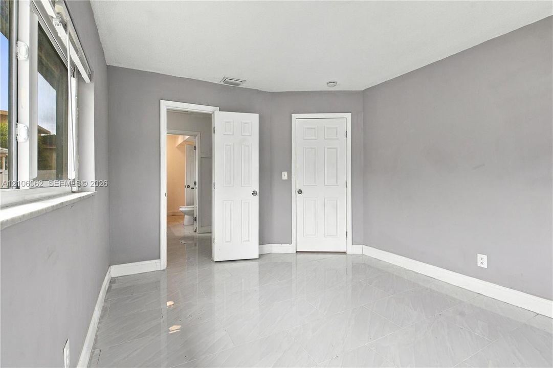 Room featuring gray walls, polished tile flooring, two white panel doors, and a double-hung window with a sill