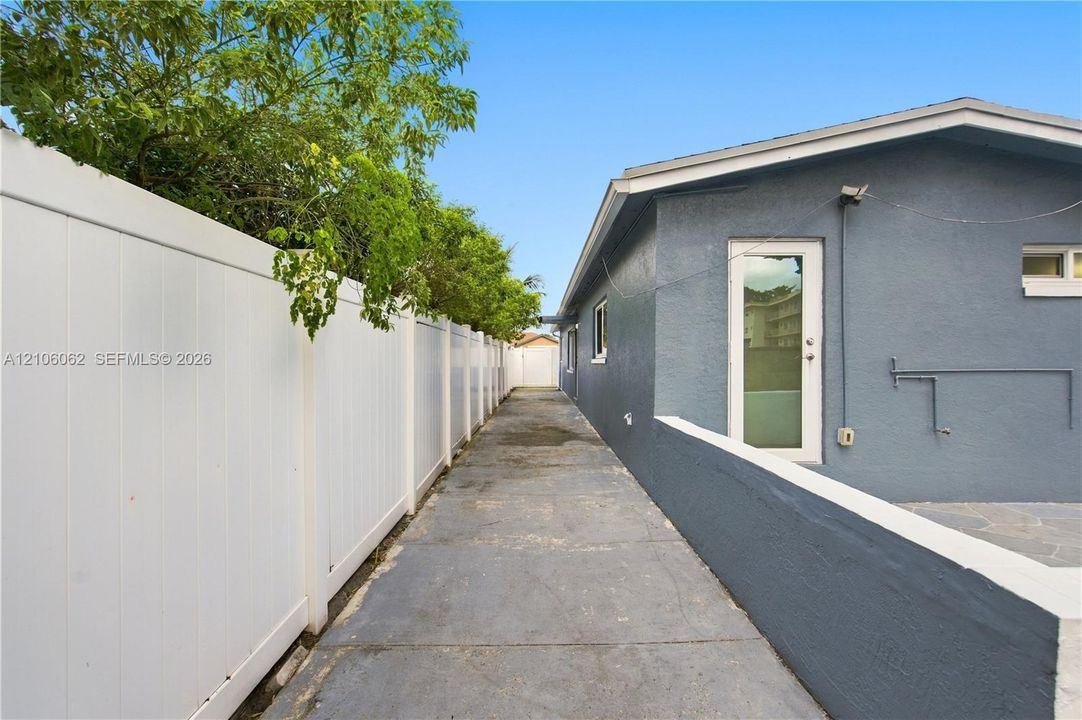 Exterior side pathway featuring a concrete walkway, white privacy fencing, and a stucco-finished exterior wall