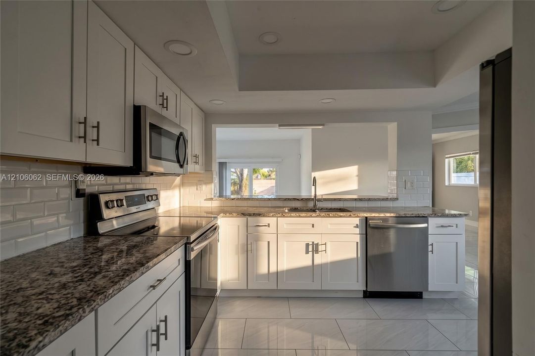 Kitchen featuring white shaker-style cabinetry, stone-finish countertops, stainless steel appliances, a white subway tile backsplash, and large-format tile flooring