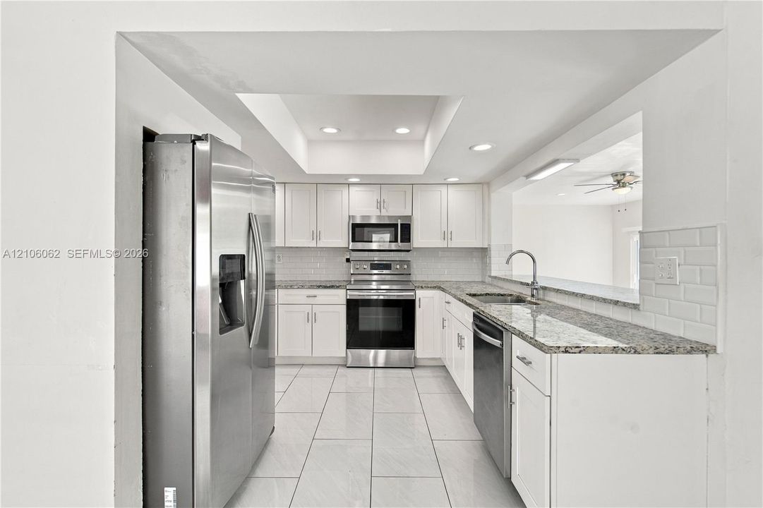 Kitchen featuring white cabinetry, stone-finish countertops, stainless steel appliances, recessed tray ceiling lighting, and tiled flooring