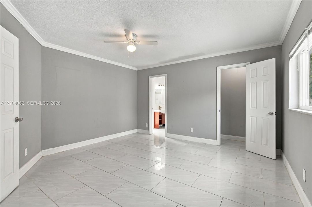 Interior room featuring large-format ceramic tile flooring, neutral grey wall paint, crown molding, and a ceiling-mounted light fixture with an integrated fan