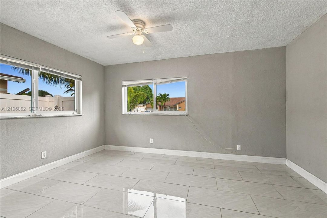 Light-filled interior featuring large-format ceramic tile flooring, neutral wall finishes, multiple dual-pane windows, and a central ceiling fan with integrated lighting
