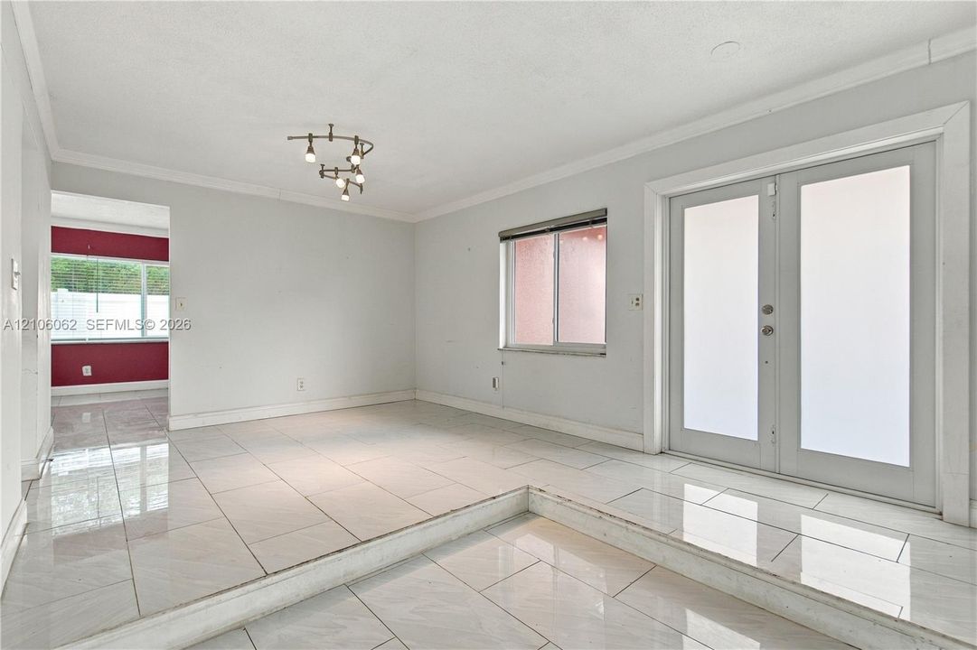 Sunken living area featuring large-format ceramic tile flooring, multi-light modern ceiling fixture, frosted glass double doors, and crown molding
