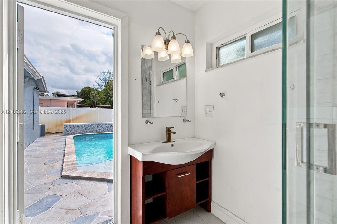 Vanity featuring wood-finish cabinetry, a white integrated basin, and a metallic faucet, complemented by a five-light vanity fixture, a rectangular mirror, and a glass-enclosed shower