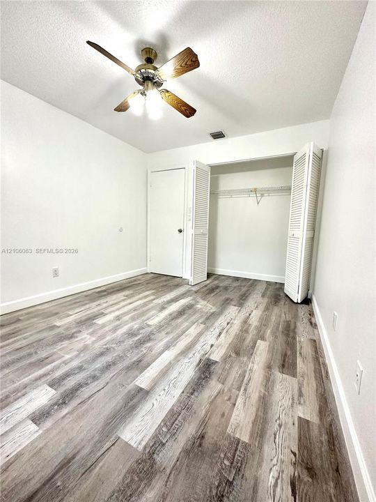 Room featuring wood-finish flooring, a ceiling fan with integrated lighting, and a closet with louvered doors