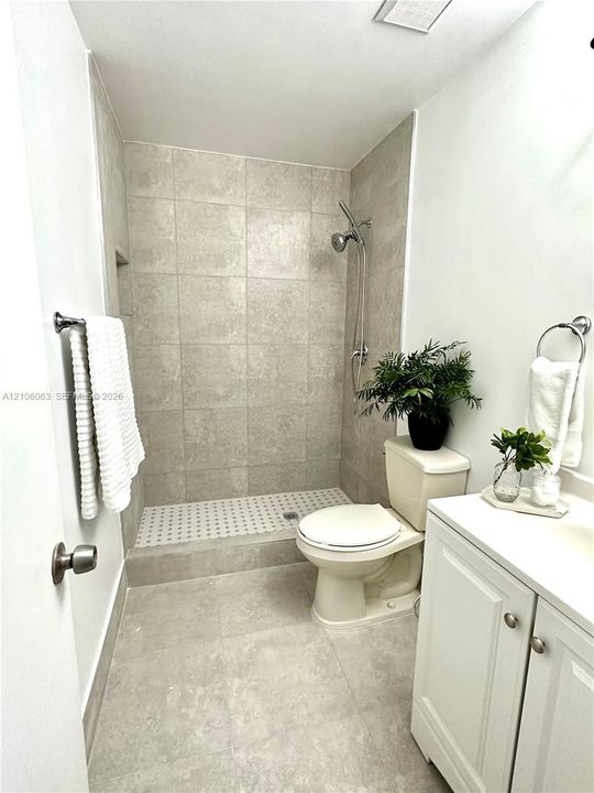 Walk-in shower with large-format wall tile, mosaic tile shower floor, and adjustable handheld showerhead, complemented by a white vanity cabinet