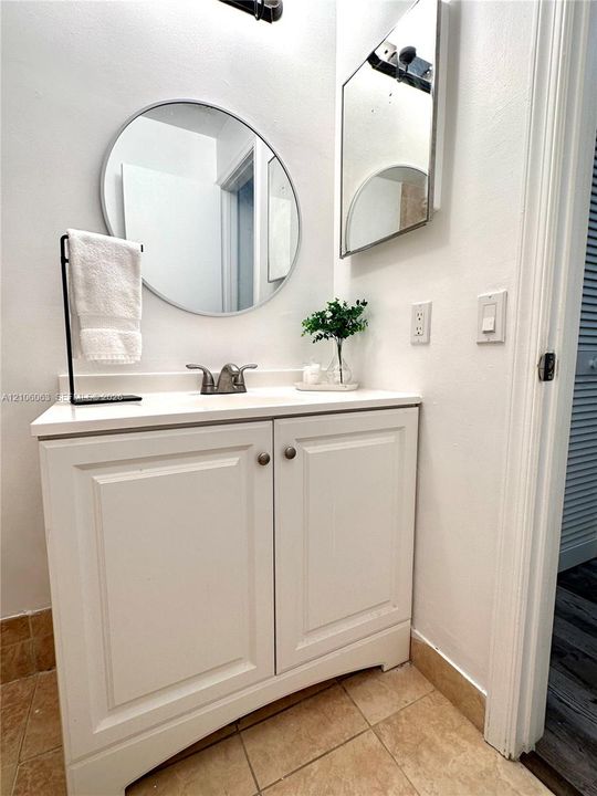 White cabinetry vanity with a solid-surface countertop, center-set faucet, circular wall mirror, and tile flooring