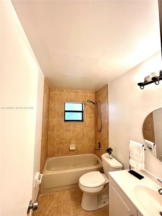 Bathroom featuring a porcelain tub with tile surround, vanity with an integrated sink, wall-mounted light fixture, and oval mirror
