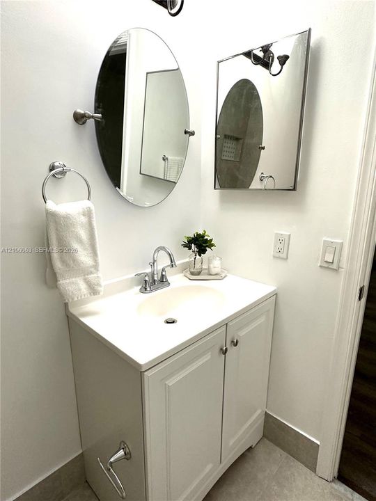 Bathroom vanity featuring a white cabinet base, integrated sink, chrome dual-handle faucet, oval tilting mirror, and wall-mounted metal towel ring