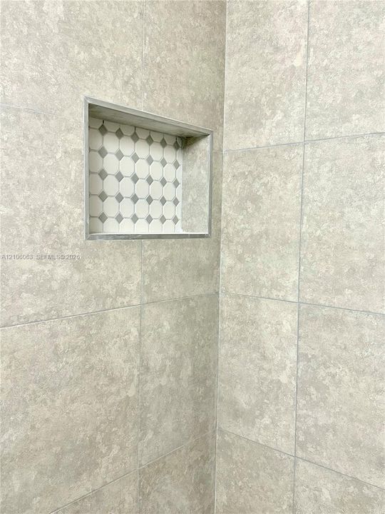 Large-format neutral wall tile featuring a recessed storage niche with decorative geometric mosaic inlay and metal trim