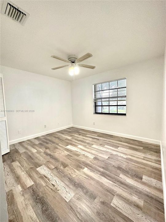 Room featuring wood-finish flooring, a multi-blade ceiling fan with integrated lighting, and a single-pane window with grid muntins