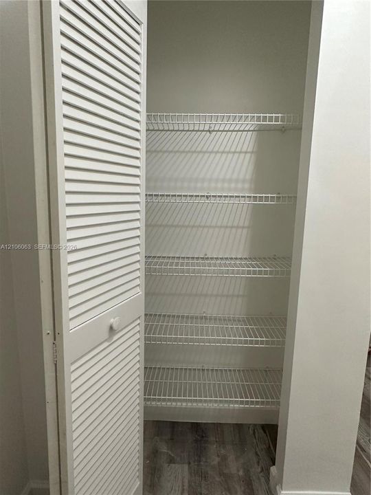 Storage closet featuring white louvered doors and five tiers of white wire shelving