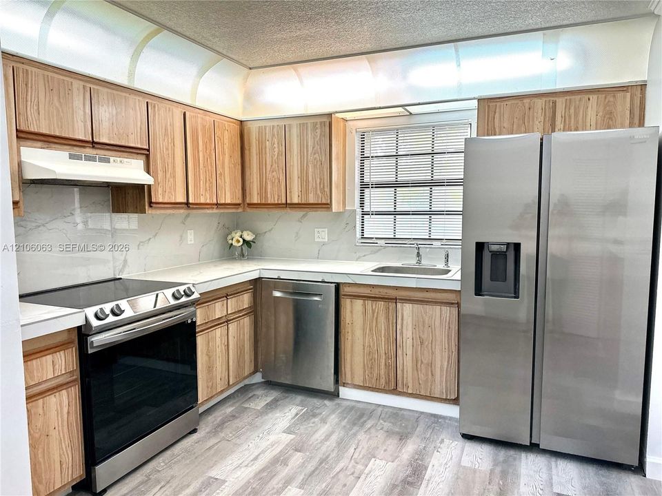Kitchen featuring wood-finish cabinetry, stone-patterned backsplash, stainless steel appliances, and wood-finish flooring