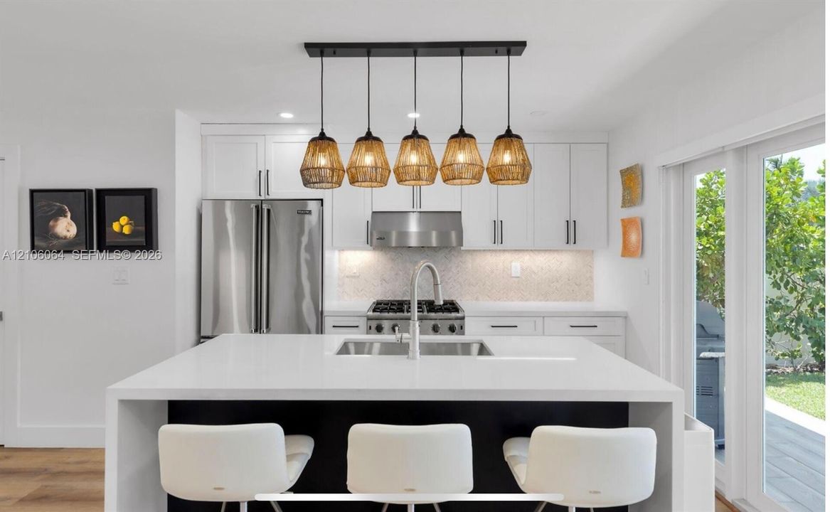 Kitchen featuring a central island with a solid surface countertop, white shaker-style cabinetry, stainless steel professional-grade appliances, and a linear multi-pendant lighting fixture