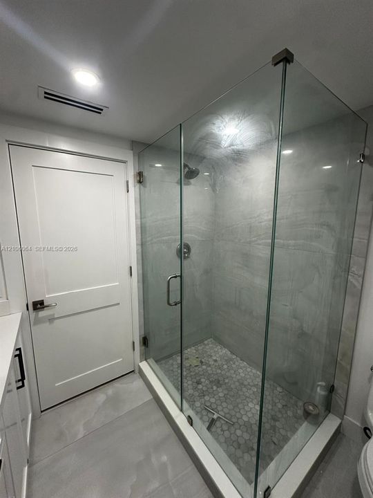 Walk-in shower featuring a frameless glass enclosure, floor-to-ceiling stone-patterned tile surround, and mosaic tile flooring