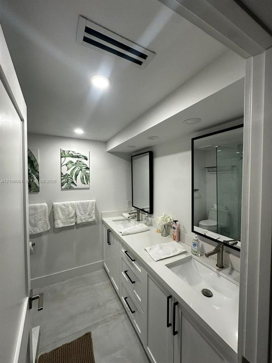 Dual-sink vanity featuring white cabinetry, solid-surface countertops, integrated rectangular basins, and matte black fixtures, complemented by recessed lighting and framed vanity mirrors
