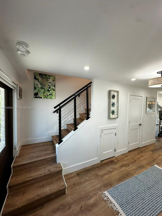 Staircase featuring wood-finish treads, a black metal handrail, and horizontal cable balusters, complemented by wood-finish flooring, recessed lighting, and white shaker-style doors