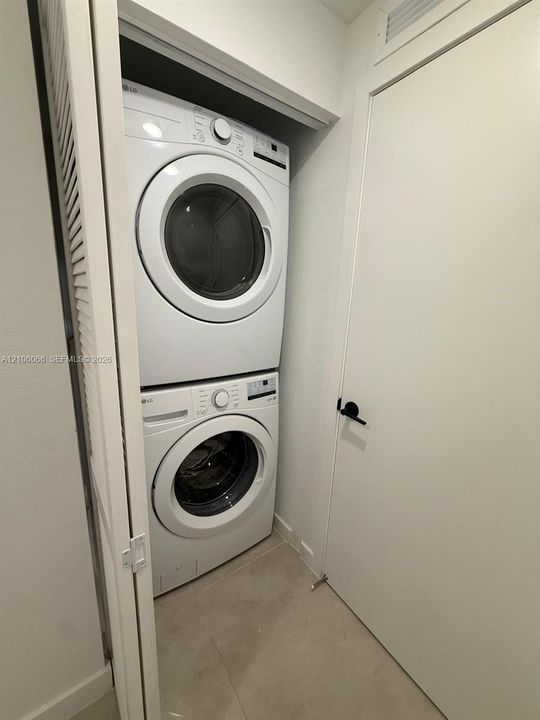 Dedicated laundry closet featuring a stackable washer and dryer, tile flooring, and a white paneled door with matte black hardware