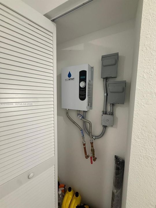 Tankless electric water heater featuring a digital temperature control interface, wall-mounted configuration, and metal conduit electrical housing