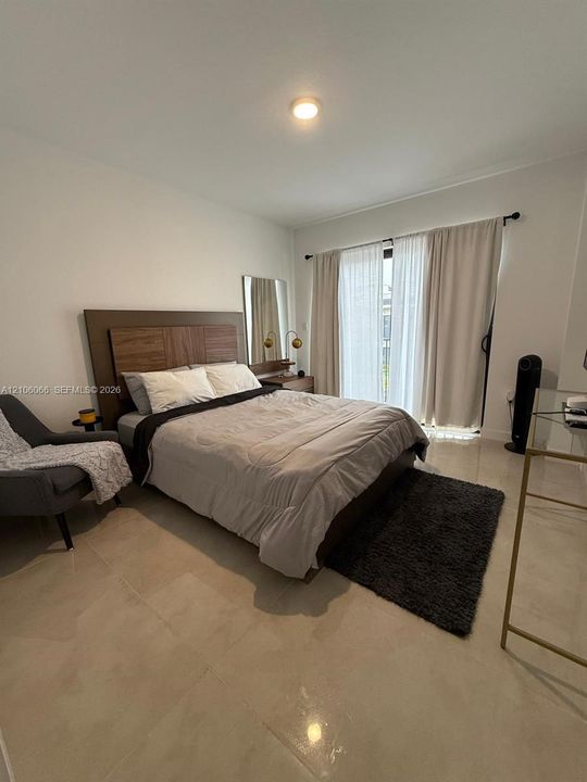 Neutral-toned large format tile flooring, sliding glass door with dual-track curtain hardware, and flush-mount ceiling lighting