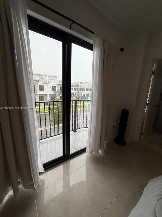 Full-height glass door with black frame, tiled flooring, and a private balcony featuring a black metal railing
