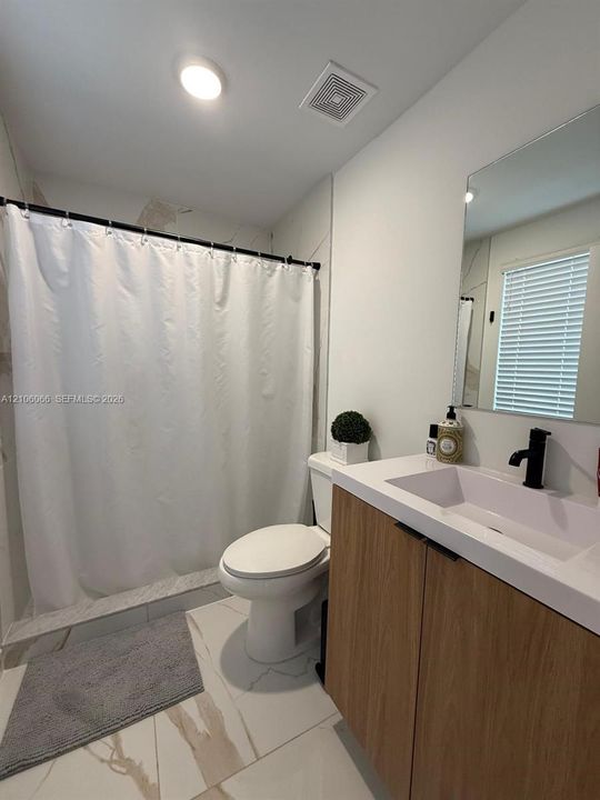 Modern floating vanity featuring wood-finish cabinetry, a white rectangular sink, and a matte black faucet, complemented by large-format white tile flooring with neutral veining and a wall-mounted mirror