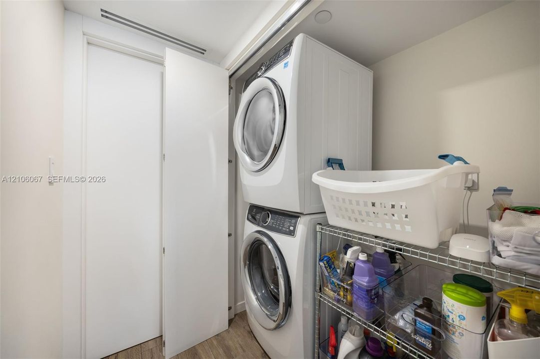 Laundry closet featuring a stacked washer and dryer unit, flat-panel door, and wood-finish flooring