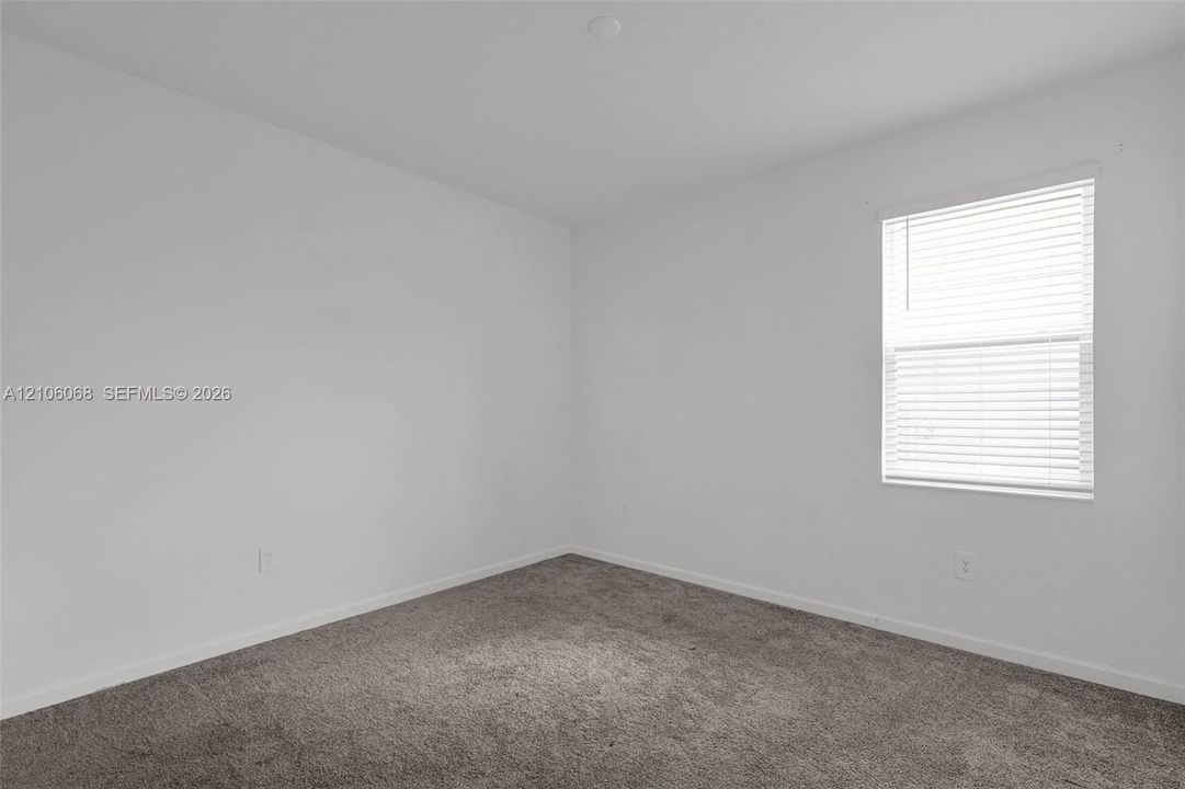 Neutral interior room featuring plush carpeting, white walls, and a window with horizontal blinds