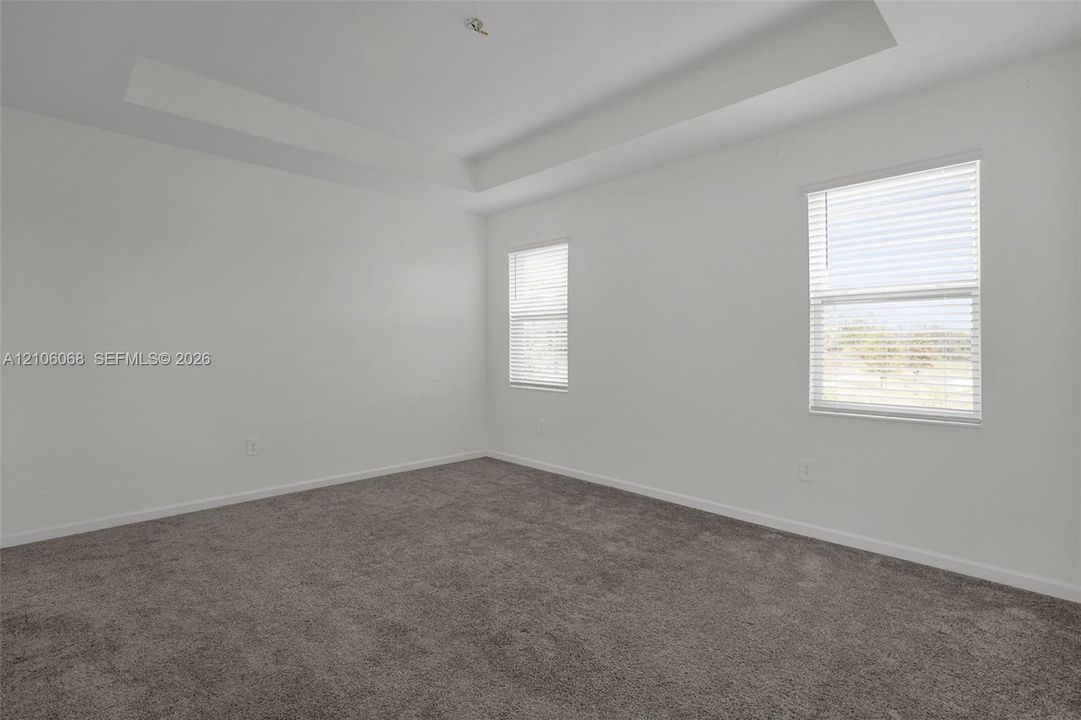 Interior room featuring a tray ceiling, wall-to-wall carpeting, and dual windows with fitted blinds