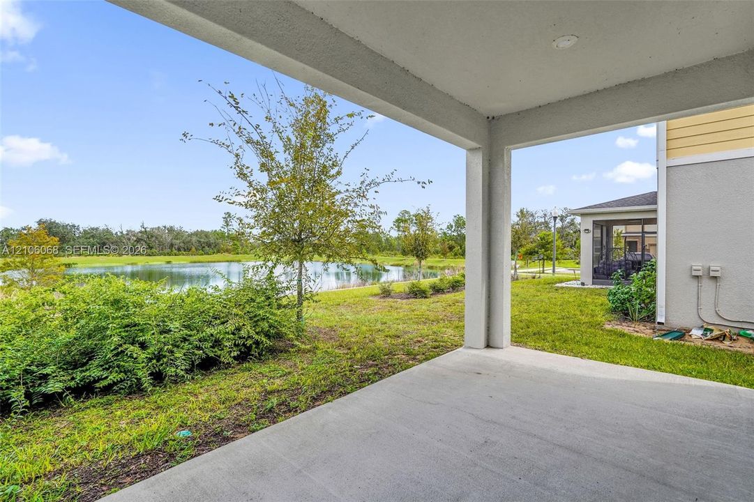 Covered concrete patio featuring a water frontage, exterior stucco finish, and landscaped grounds