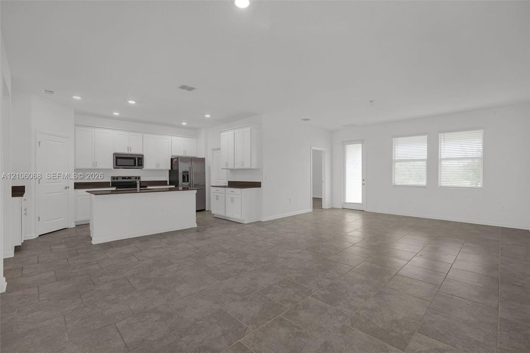 Open-concept interior featuring large-format tile flooring, recessed lighting, white cabinetry, a kitchen island with stone-surface countertops, and multiple windows
