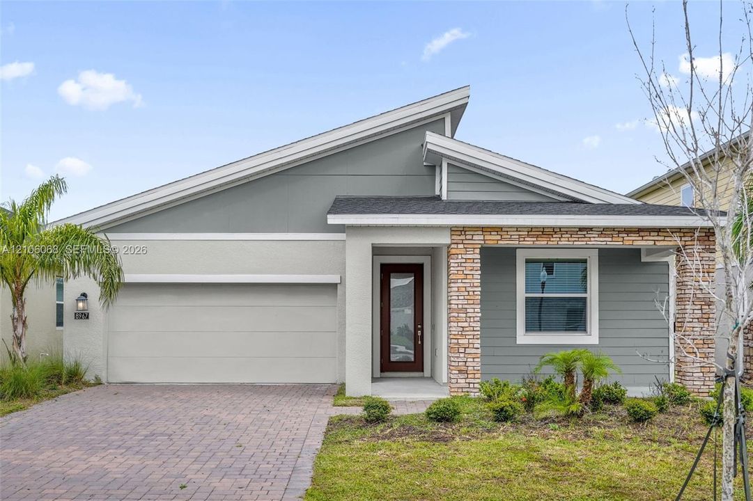 Modern single-story exterior featuring a shed roofline, stone veneer accents, horizontal siding, and a paver driveway