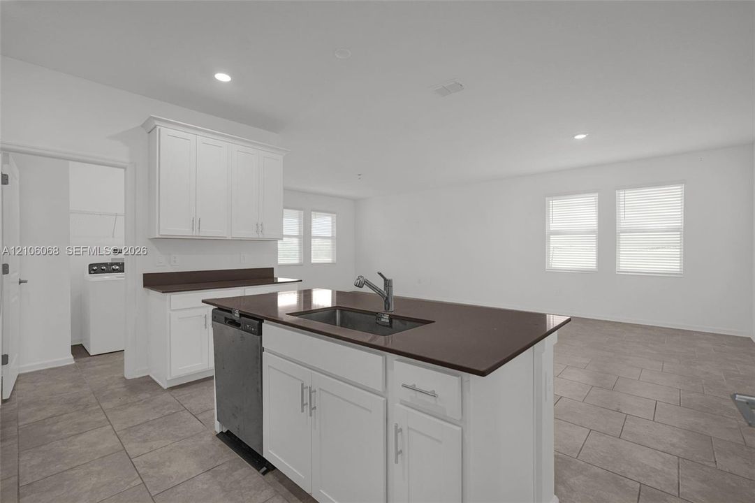 Kitchen featuring white cabinetry, solid-surface countertops, center island with an integrated stainless steel sink, recessed lighting, and tile flooring
