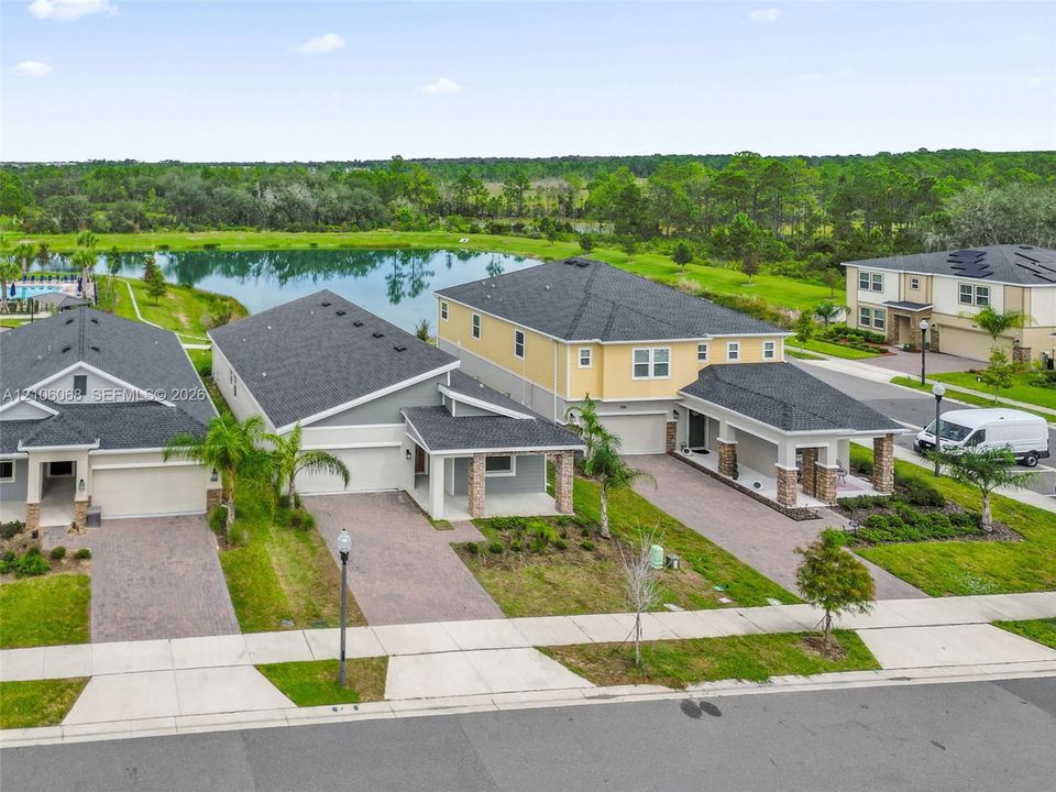 Aerial view featuring two-story residences with asphalt shingle roofing, paved driveways, covered front porches with stone-clad columns, and immediate pond frontage